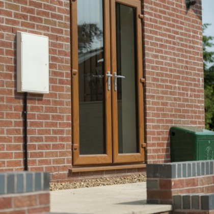 White electrical box next to woodgrain uPVC French doors