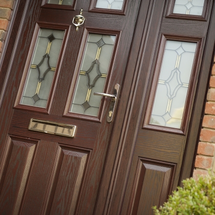 Rosewood uPVC door in brick house with plant to the right